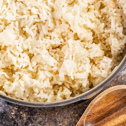 Bot of rice pilaf next to a wooden spoon.