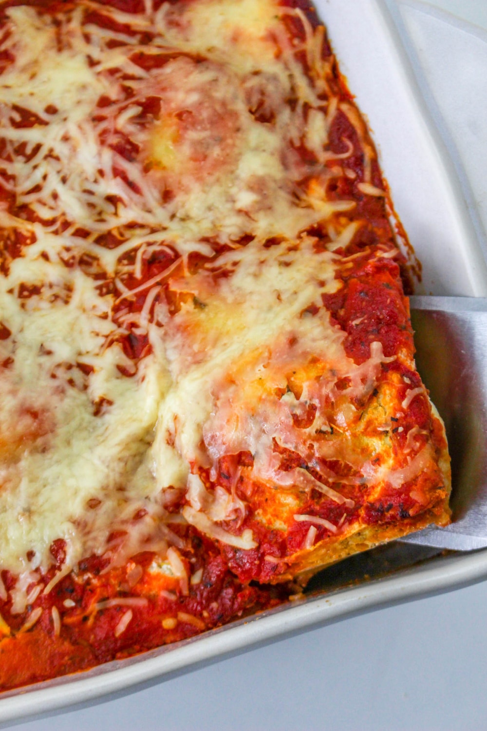 Serving utensil scooping Baked Ravioli Lasagna from a baking dish.