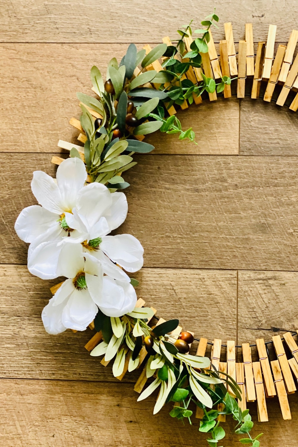 Clothes Pin Wreath with magnolia flowers and greenery on a wooden background.