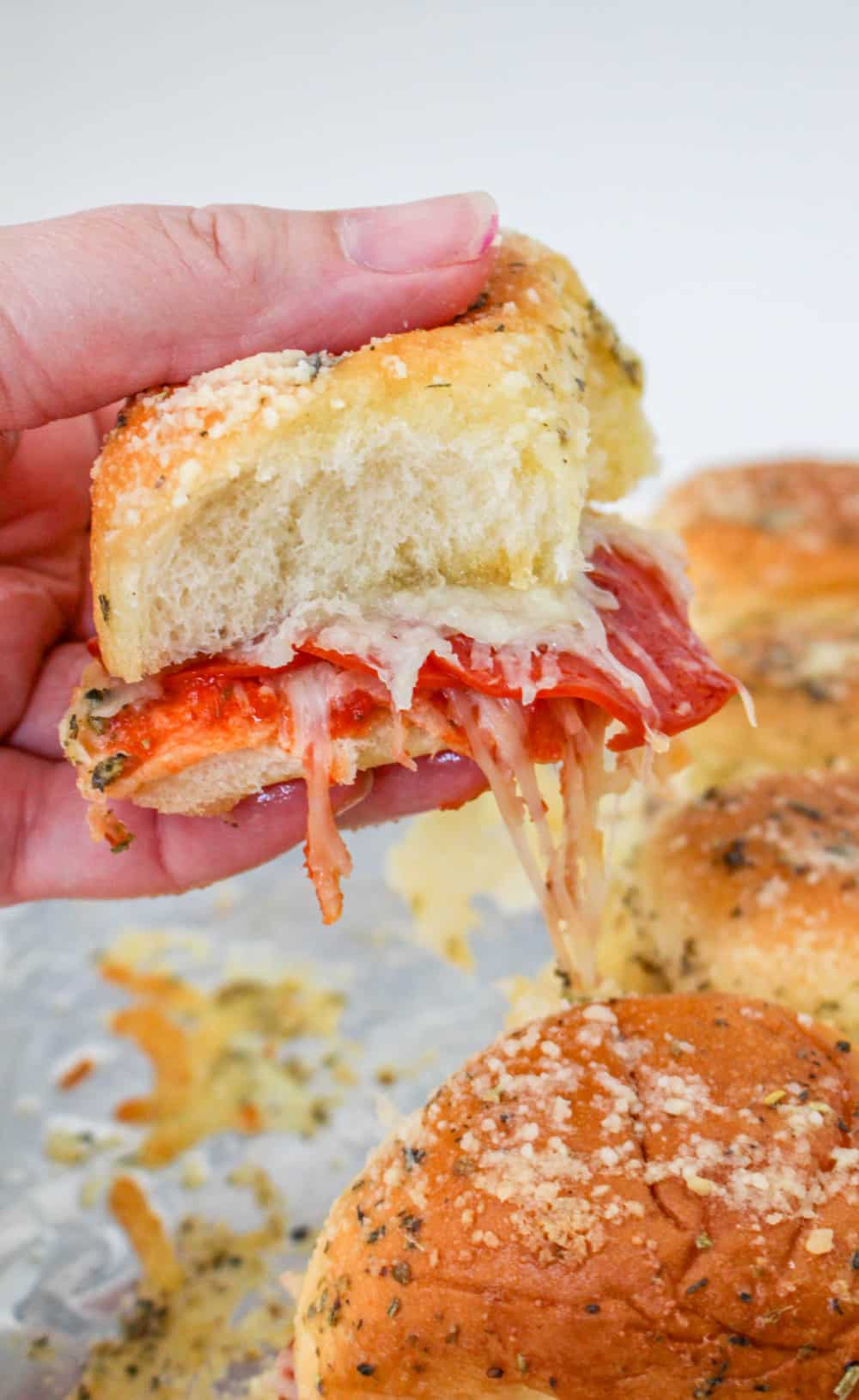 Hand holding a cheesy Pepperoni Pizza Slider.