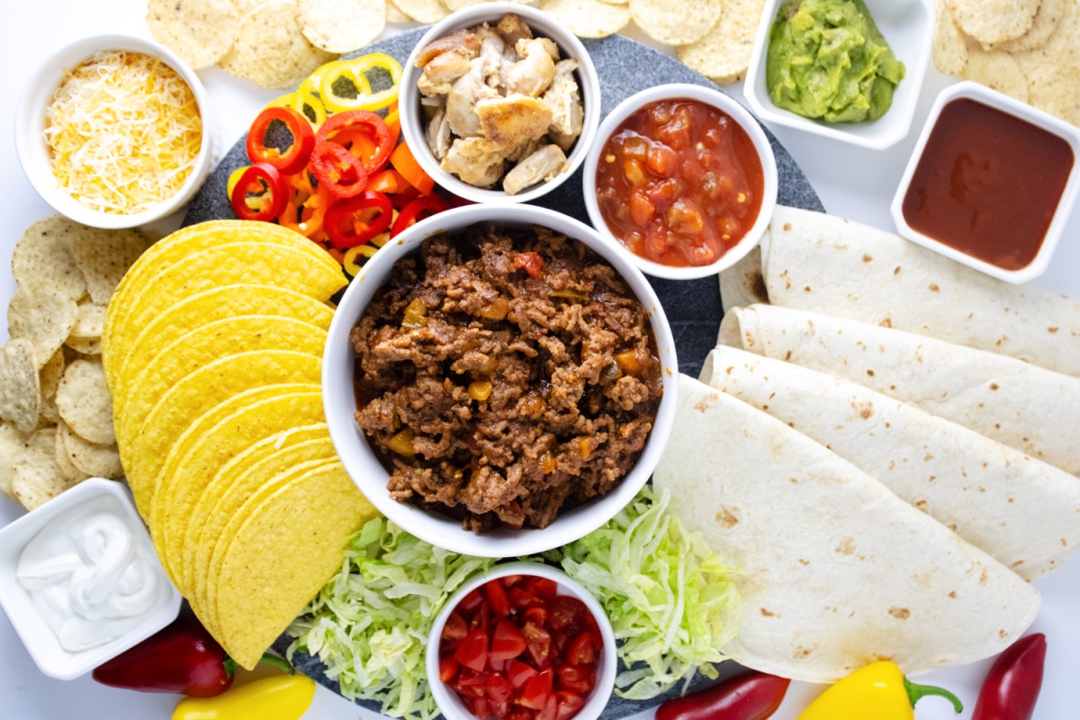 Taco Board with seasoned ground beef, tortillas, salsa, and other taco toppings.
