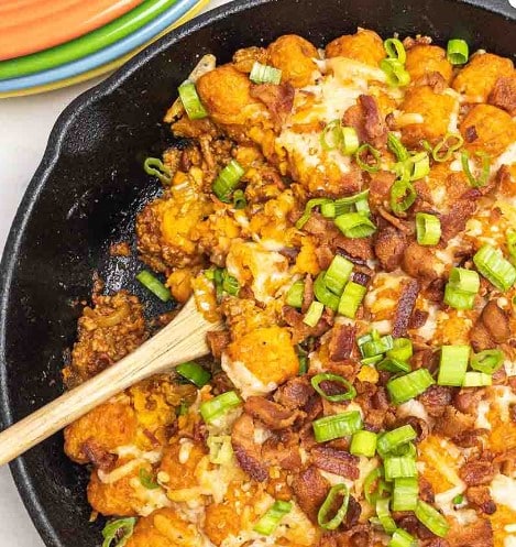 Spoon in a skillet of Bacon Cheeseburger Sweet Potato Tater Tot Casserole.
