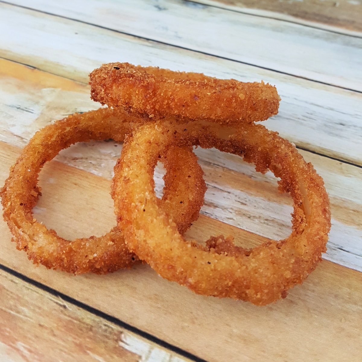 Three crispy fried Breaded Onion Rings on a countertop.
