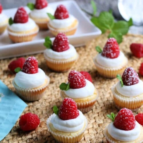 Mini cheesecakes topped with whipped cream and raspberries.
