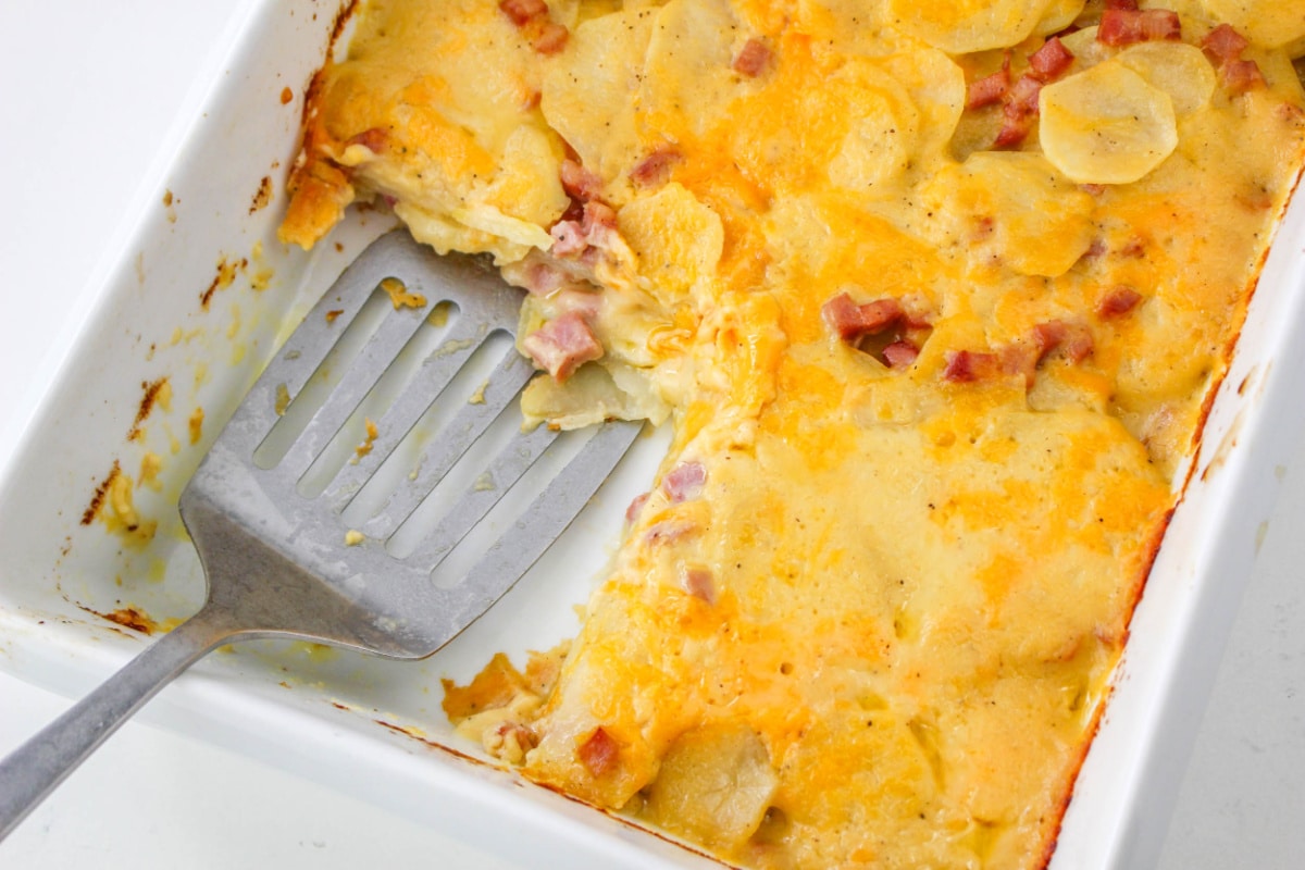 Top down view of Ham and Cheesy Scalloped Potatoes in a baking dish with a spatula.