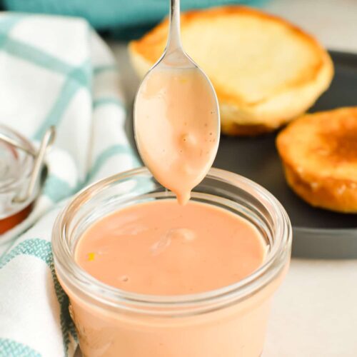 Close up of a spoon dripping burger sauce into a jar.