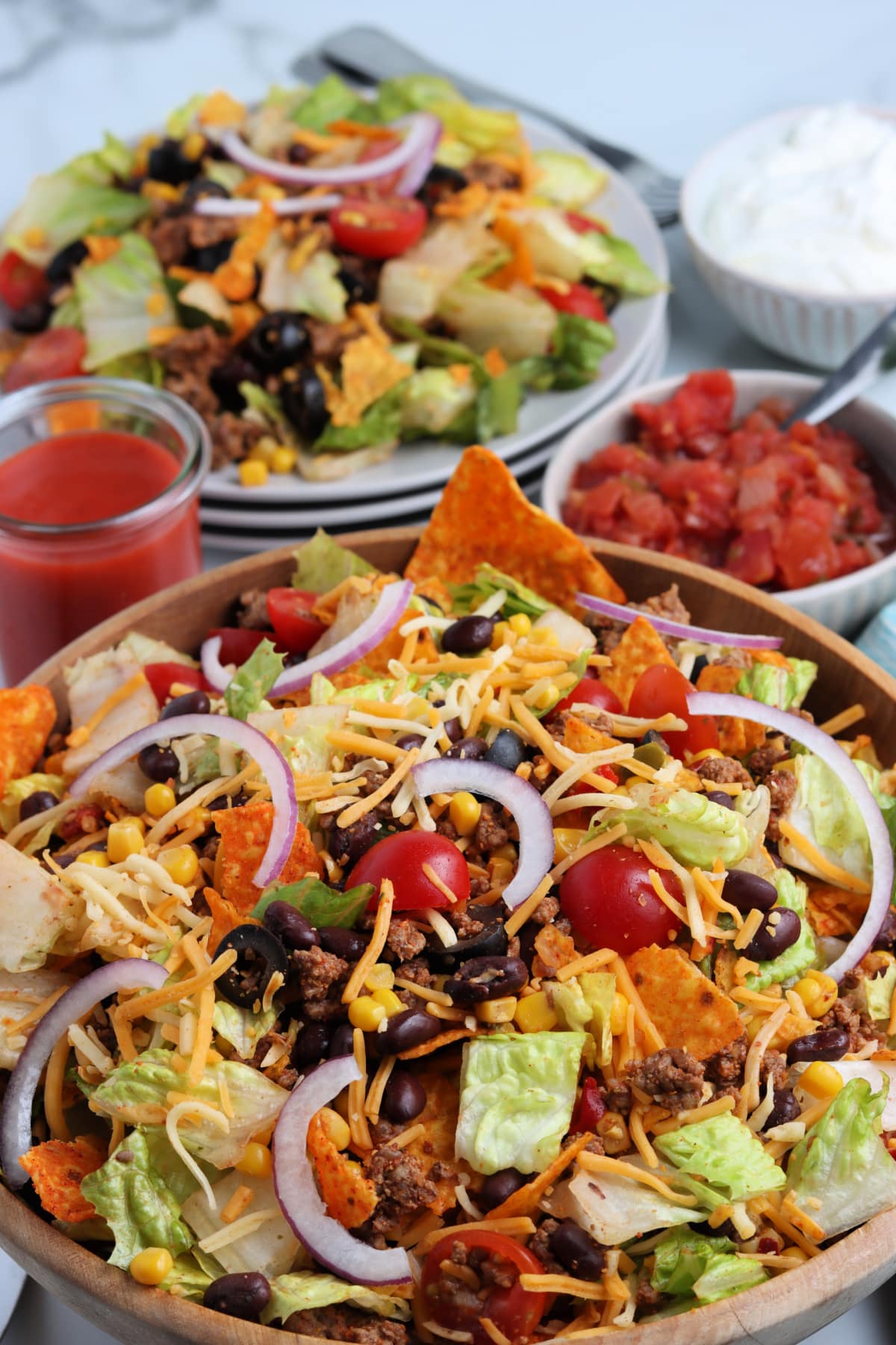 Bowl of Taco Salad with Doritos next to catalina dressing and salsa.