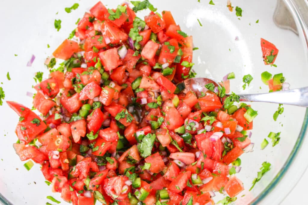 How to Make Pico de Gallo: tomatoes, onions, and other ingredients in a bowl with a spoon.
