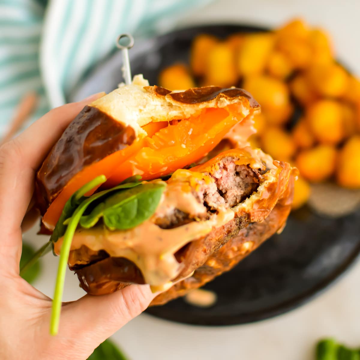 Hand holding a cheeseburger with tomatoes, spinach, and smashburger sauce.