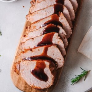 Top down sliced Pork Loin on a cutting board with brown sugar balsamic glaze.