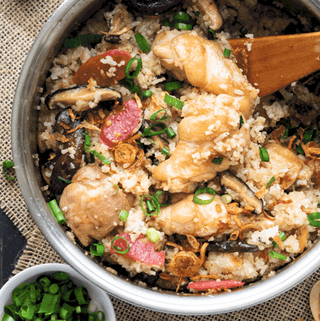 Top down view of chicken and mushroom rice in a rice cooker with a wooden spoon.
