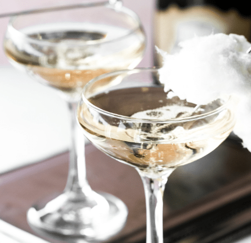 Champagne glasses topped with cotton candy on a stirring stick.