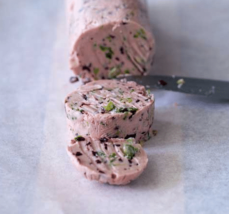 Slices of Red Wine and Shallot Butter on parchment paper with a knife.