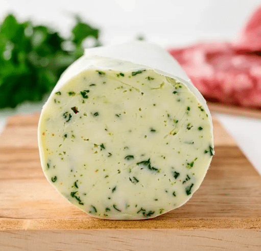 Compound Butter: Roll of Mâitre d’Hôtel Butter wrapped in parchment paper on a cutting board.