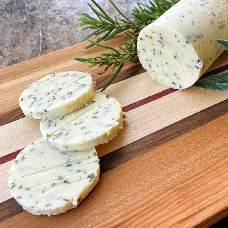 Slices of orange and herb compound butter with rosemary on a cutting board.