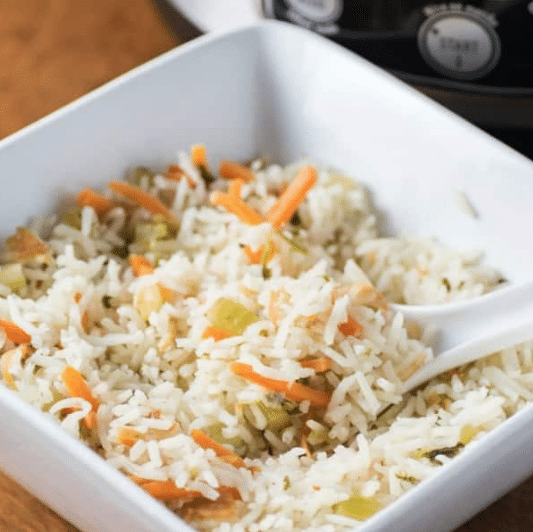 Rice pilaf with carots and celery in a serving dish with a spoon.