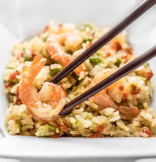 Chop sticks grabbing a piece of shrimp from a bowl of rice.