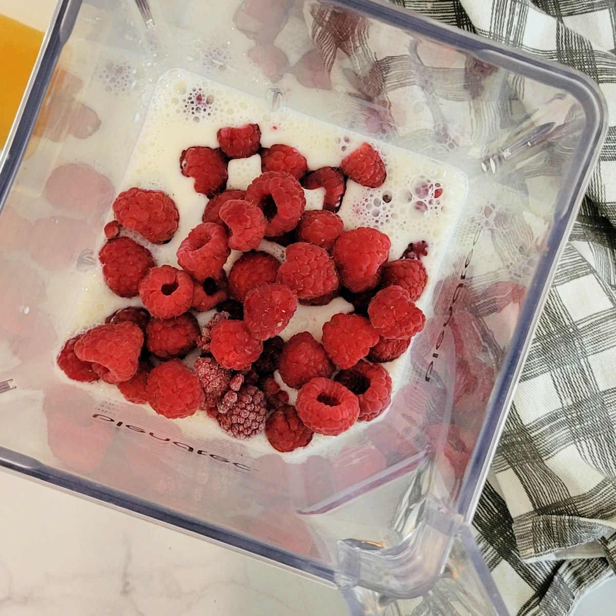 How to make a raspberry smoothie: top down close up view of raspberries and milk in a blender.