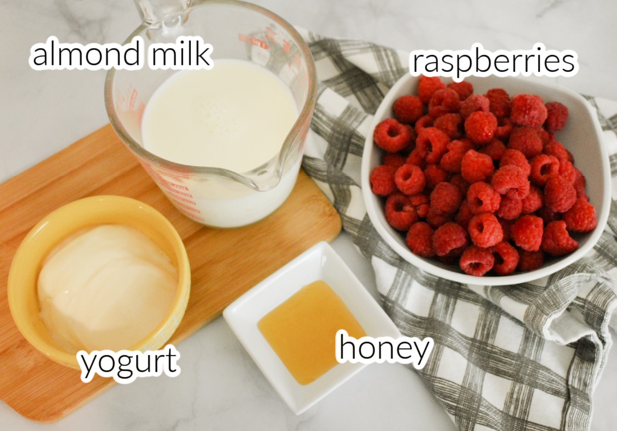 Ingredients to make a raspberry smoothie including raspberries, milk, yogurt, and honey.