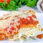 Close up of Chicken Parmesan Fettuccine Alfredo on a plate with a fork.