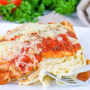 Close up of Chicken Parmesan Fettuccine Alfredo on a plate with a fork.