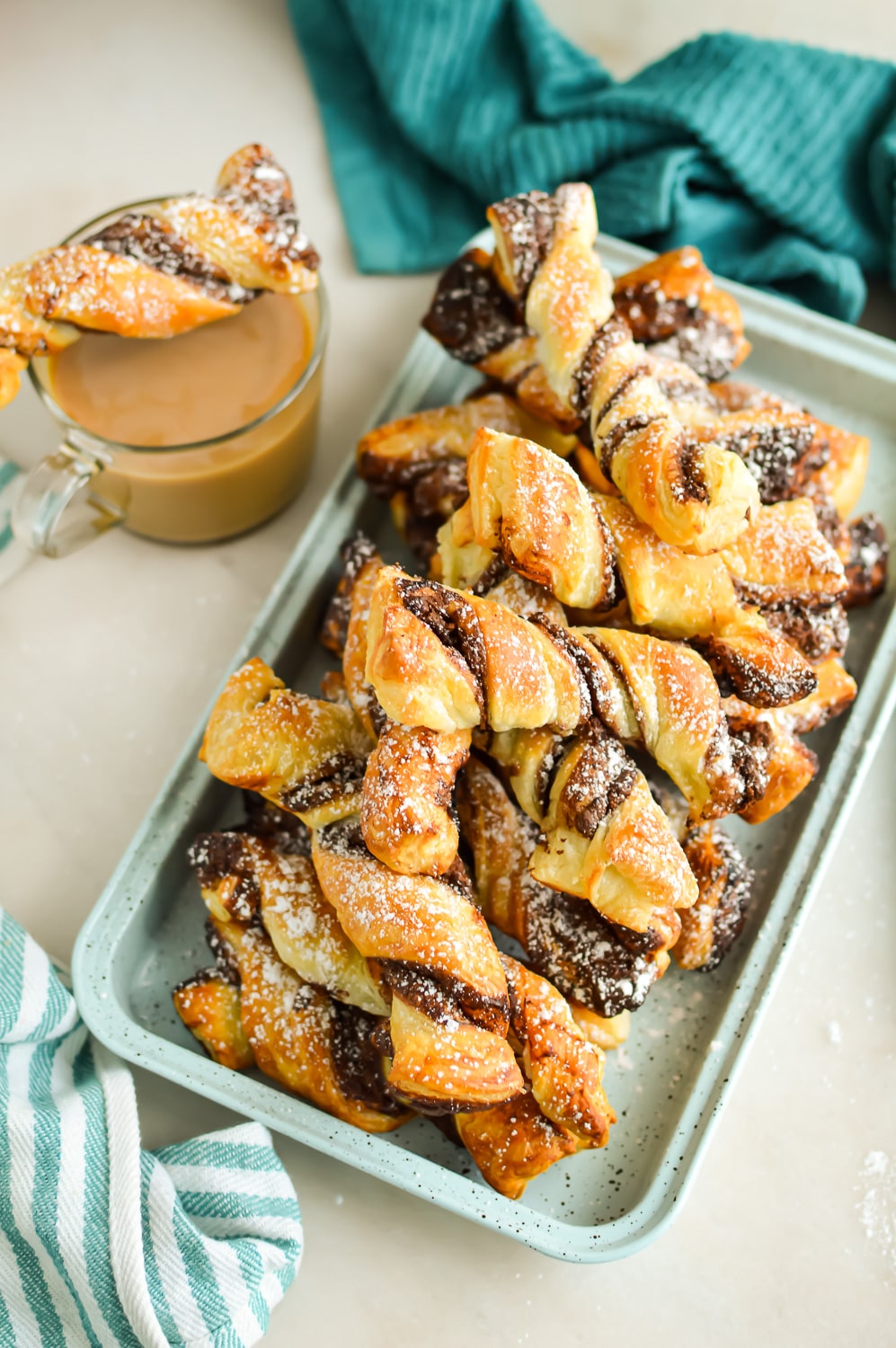 Top down view of Hazlenut and Chocolate Puff Pastry Twists dusted with powdered sugar on a serving tray next to a cup of coffee.