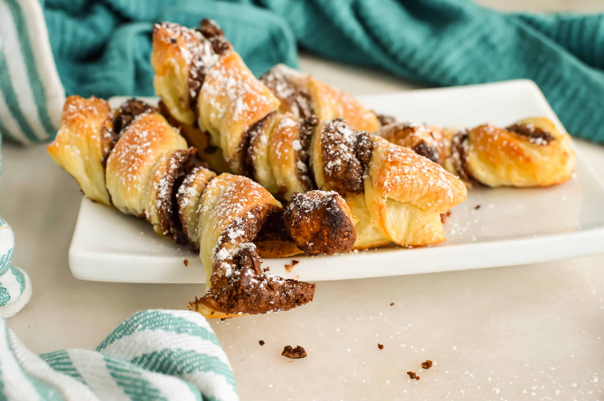 Close up of Chocolate and Hazlenut Puff Pastry Twists dusted with powdered sugar on a serving tray next to a cup of coffee.