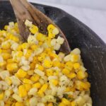 Close up of honey butter corn in a cast iron skillet with a wooden spoon.