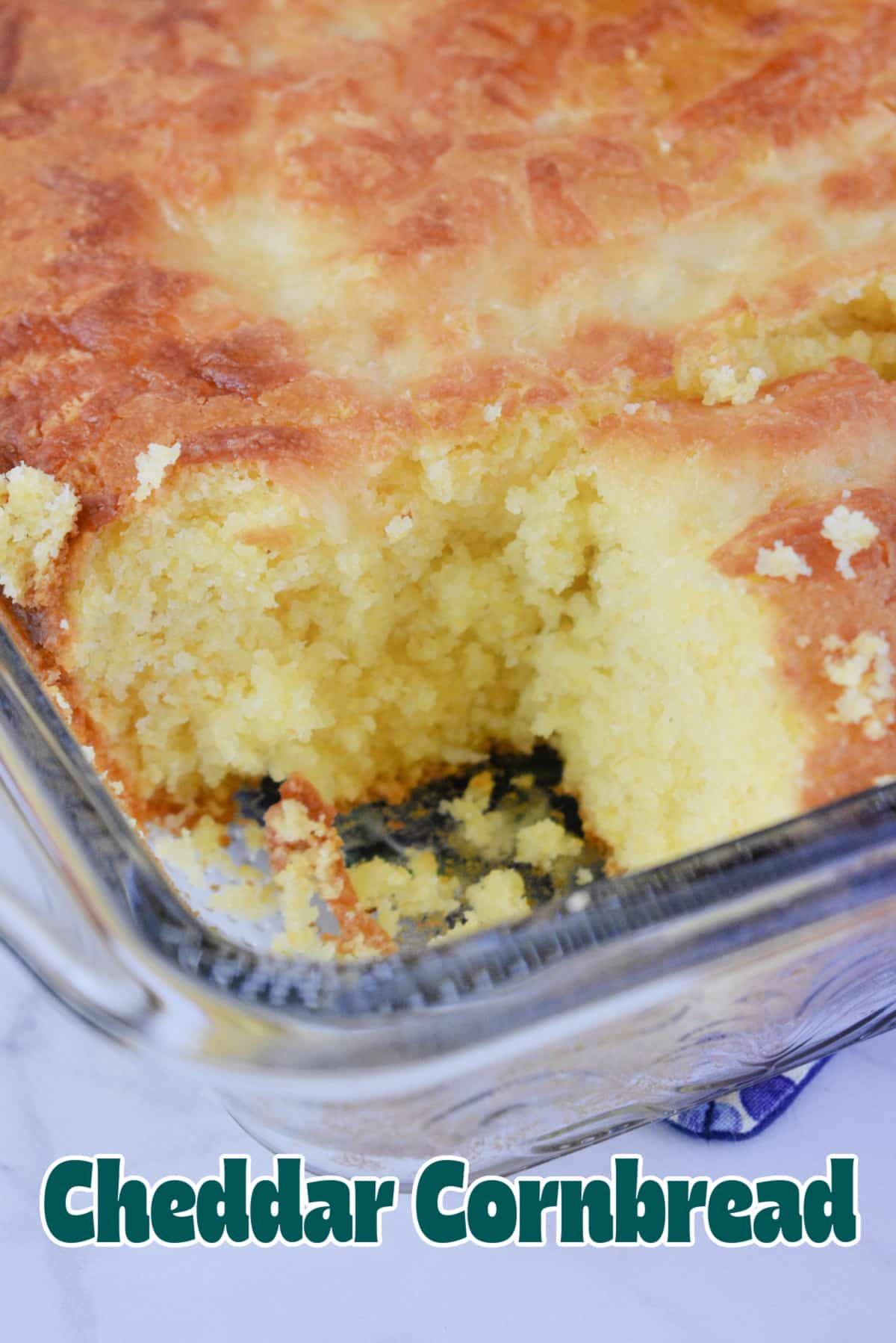 Close up of Cheddar Cornbread in a pan missing a square piece. Image has text overlay reading Cheddar Cornbread.