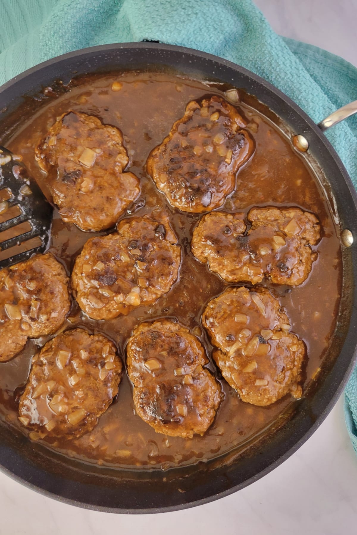 Top down view of salisbury steaks in a large skillet with gravy.