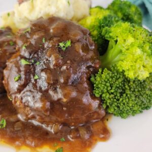 Close up of Salisbury Steak on a plate with potatoes and broccoli.
