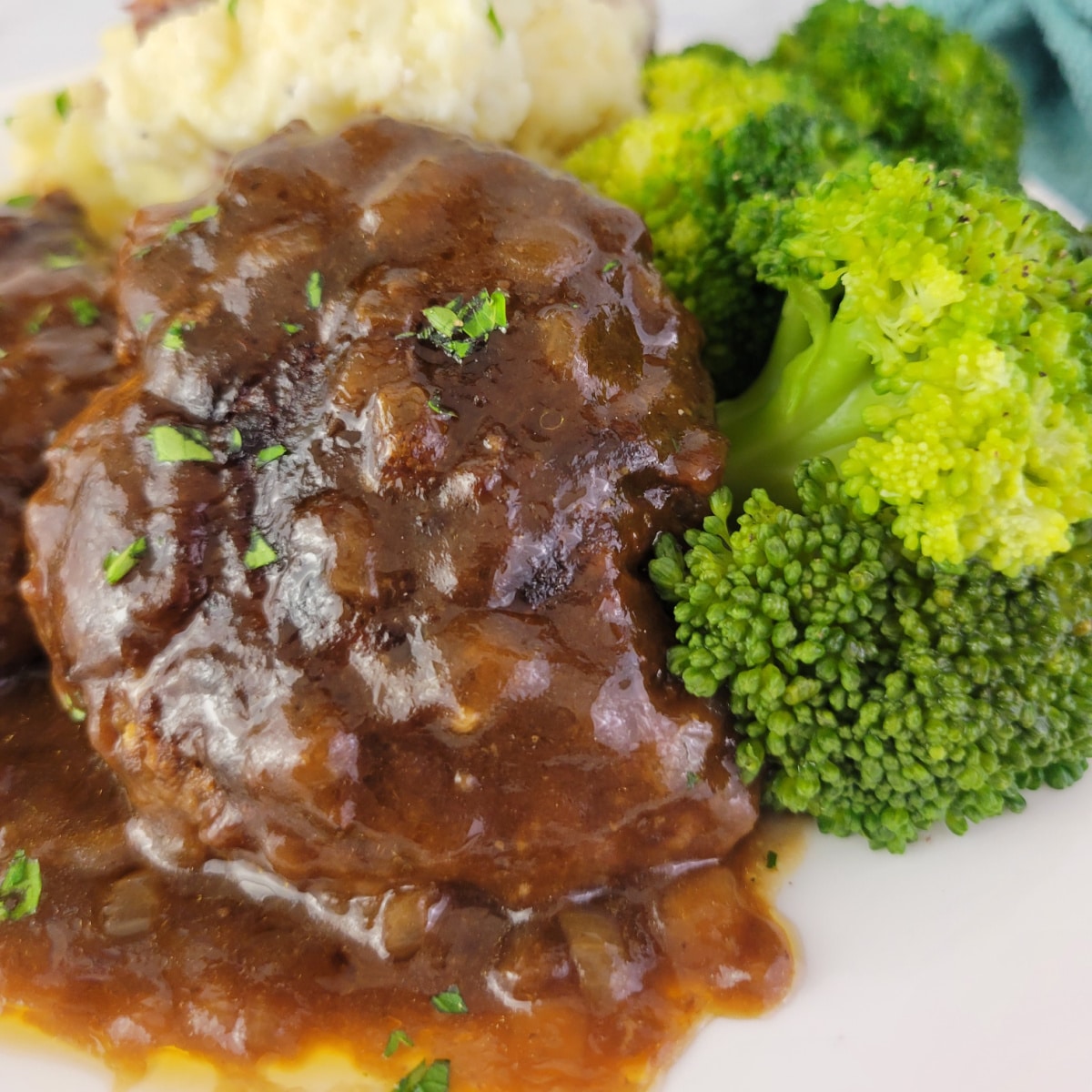 Close up of Salisbury Steak on a plate with potatoes and broccoli.
