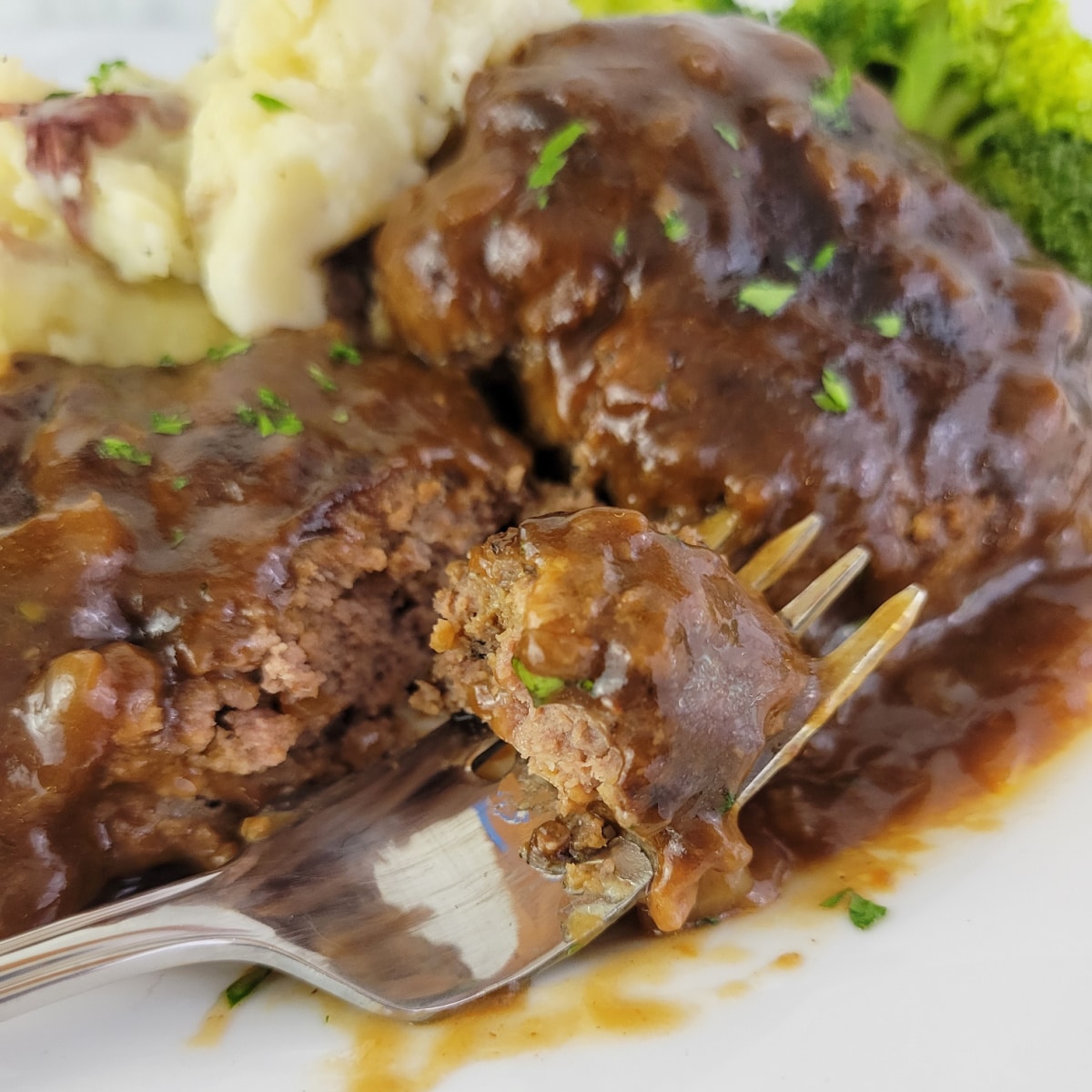 Close up of Salisbury Steak and gravy on a plate with a fork.