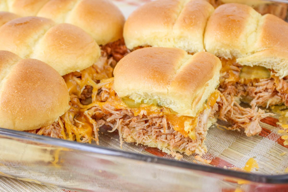 BBQ Chicken Sliders topped with cheese and pickles in a baking pan.