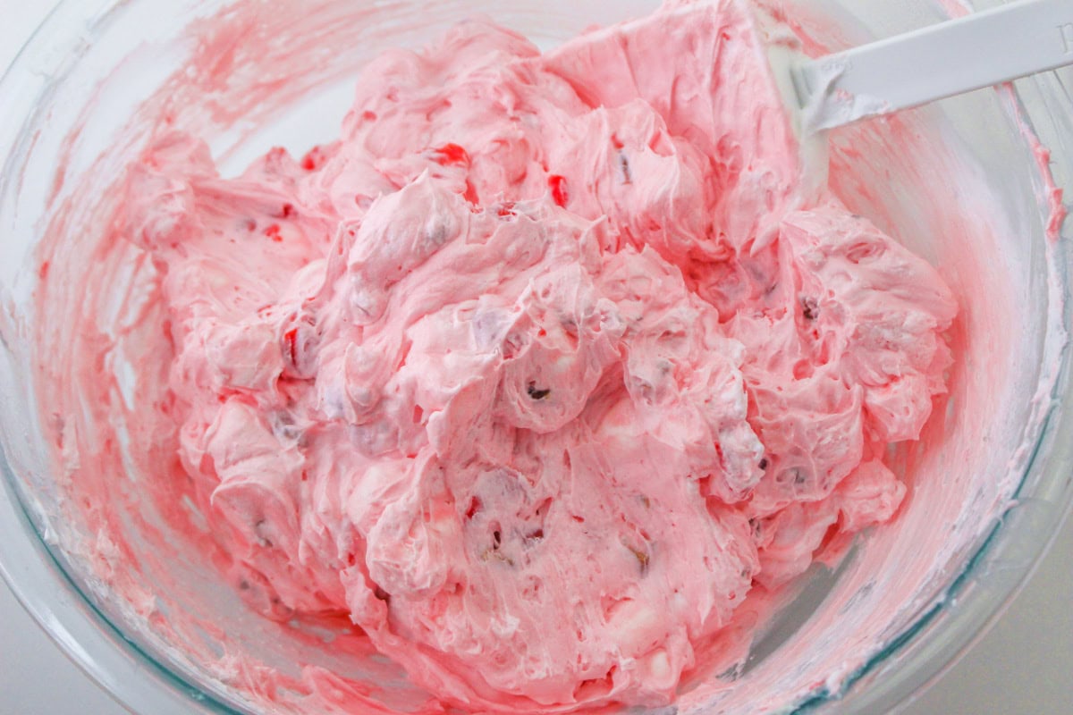 How to make Cherry Fluff: cherries folded into whipped cream in a bowl with a spatula.