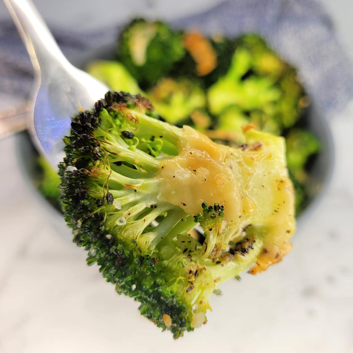 Close up of Garlic Roasted Broccoli with melted parmesan cheese on a fork.