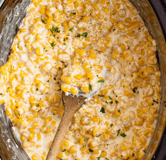 Top down view of creamed corn in a slow cooker with a wooden spoon.