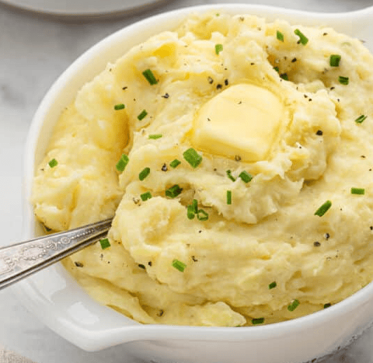 Close up of mashed potatoes in a bowl with a serving spoon.