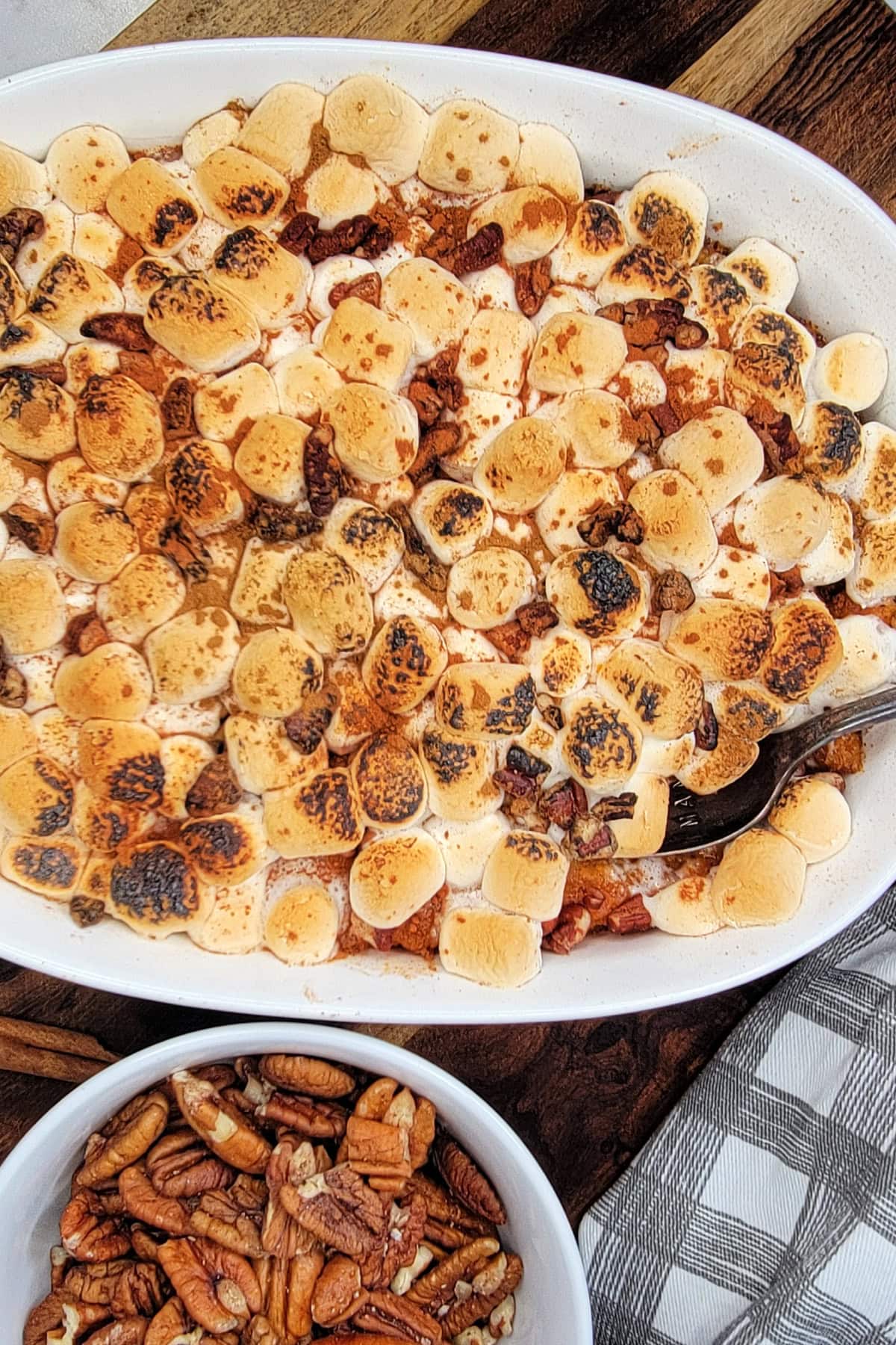 Flatlay of sweet potato casserole in a baking dish next to a small bowl of pecans.