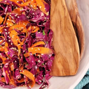 Close up of Asian Purple Cabbage Slaw with serving utensils.