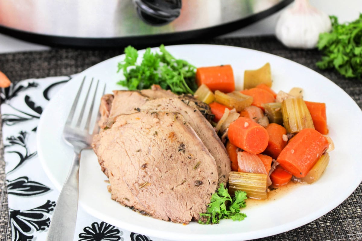Beef sirloin tip roast slow cooker recipe: slices of beef on a plate with vegetables.