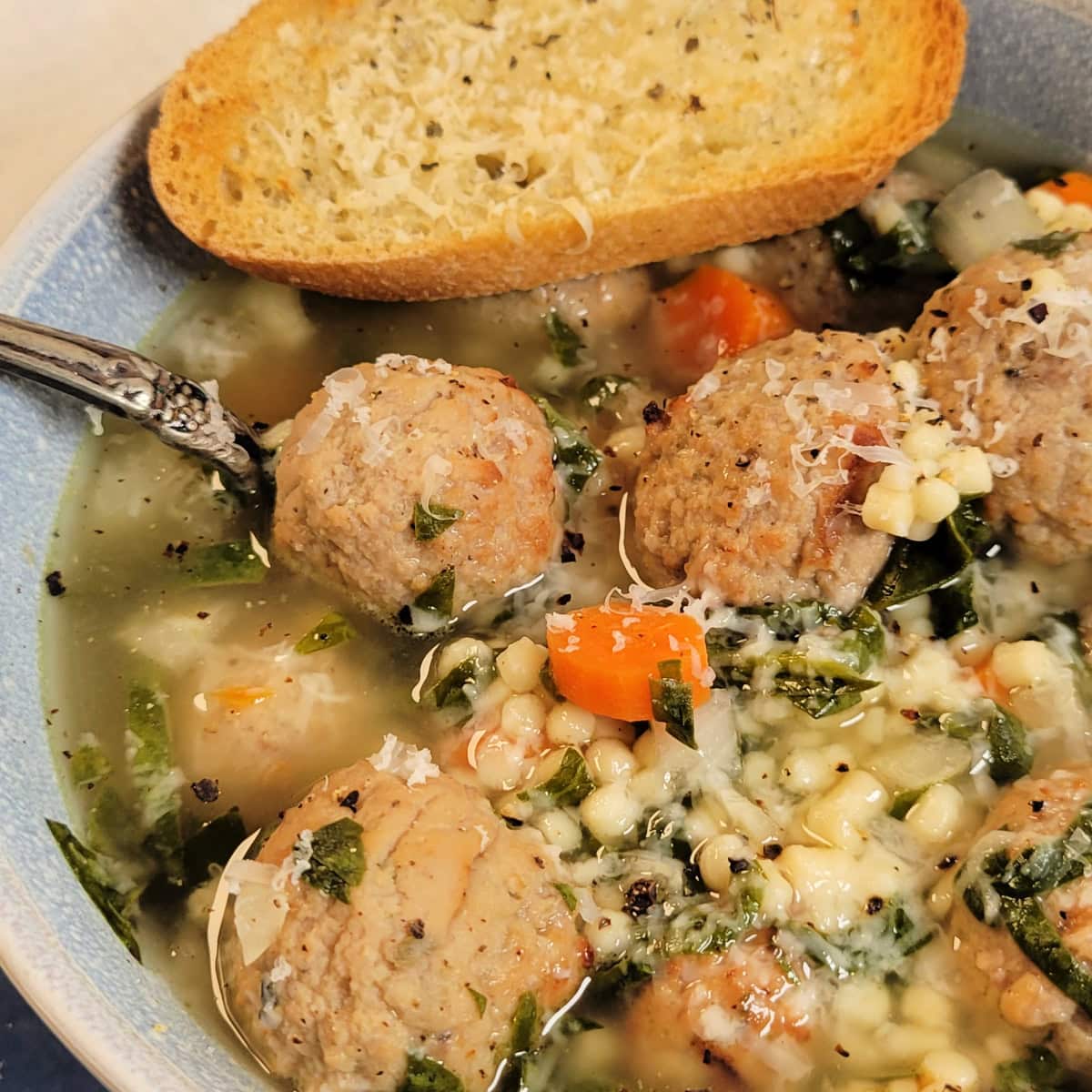 Close up of a bowl of meatball soup with garlic bread.