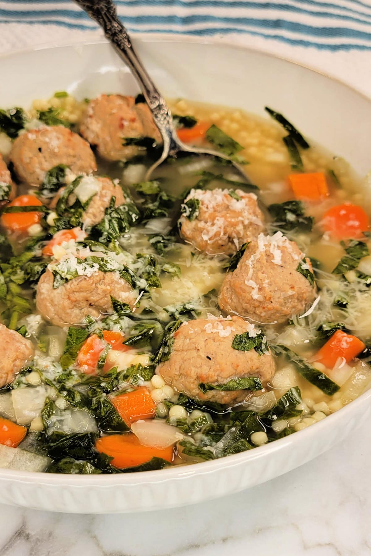 Slow Cooker Italian Wedding Soup Recipe: soup garnished with parmesan cheese in a bowl with a spoon.