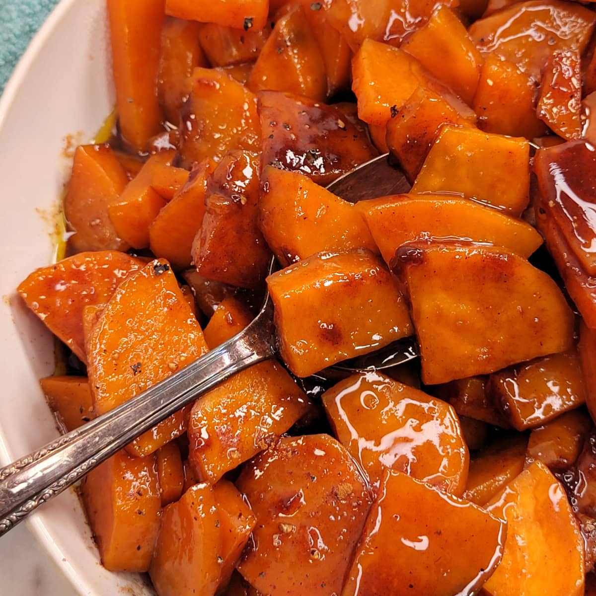 Close up of a spoon on a dish of Candied Sweet Potatoes with warm spices.