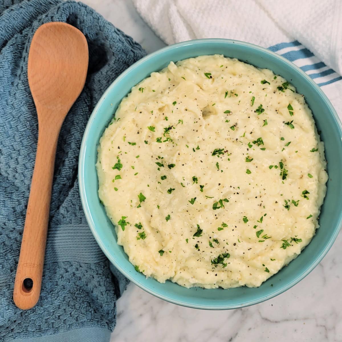 Top down view of a wooden spoon and bowl of buttery White Cheddar Mashed Potatoes.