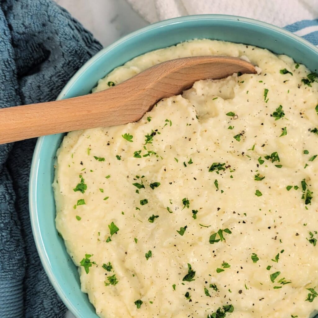 Top down view of a bowl of White Cheddar Mashed Potatoes with a wooden spoon.
