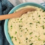 Top down view of a bowl of White Cheddar Mashed Potatoes with a wooden spoon.
