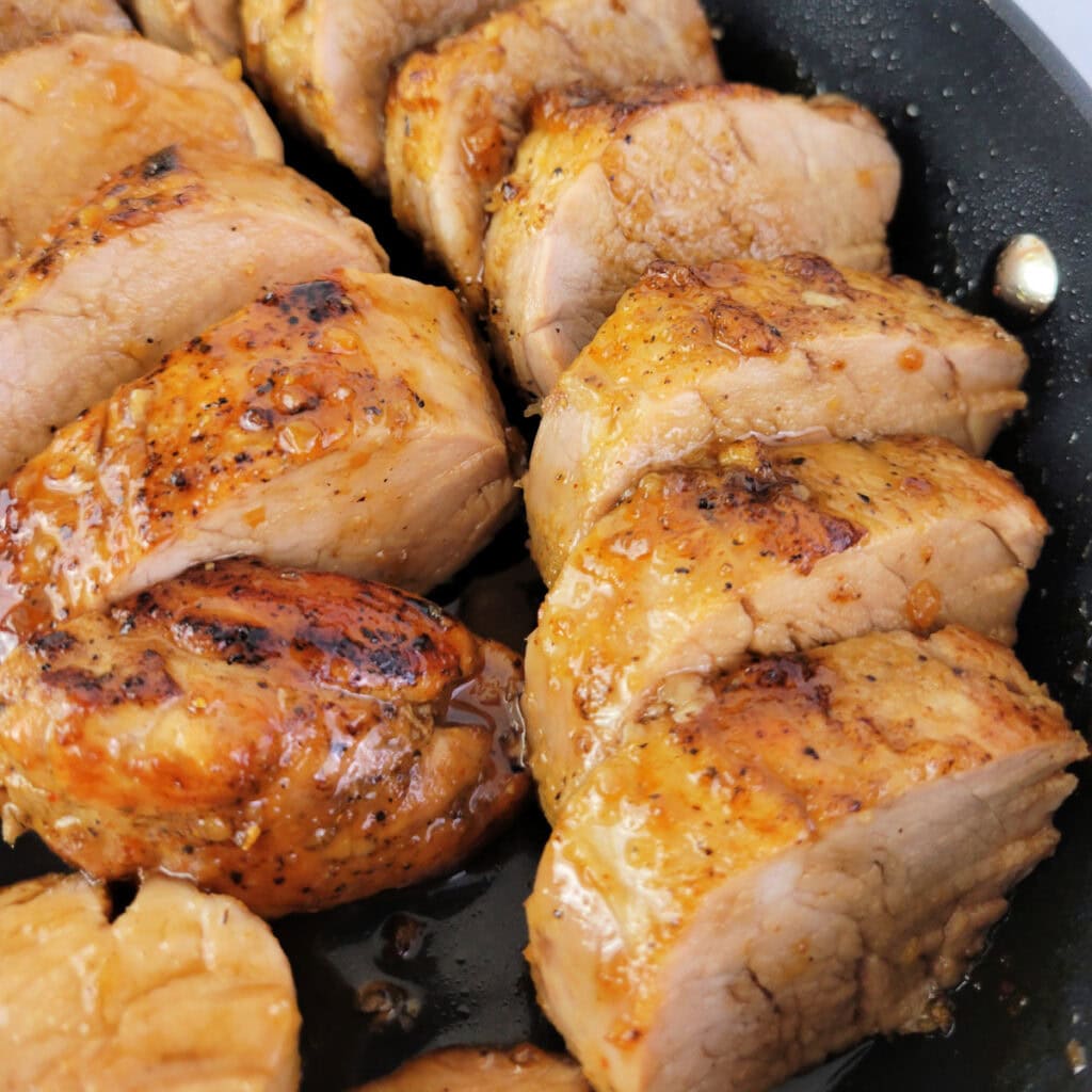 Close up of sliced honey garlic pork tenderloin in a skillet.