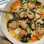 Close up of spinach and meatball soup in a bowl.