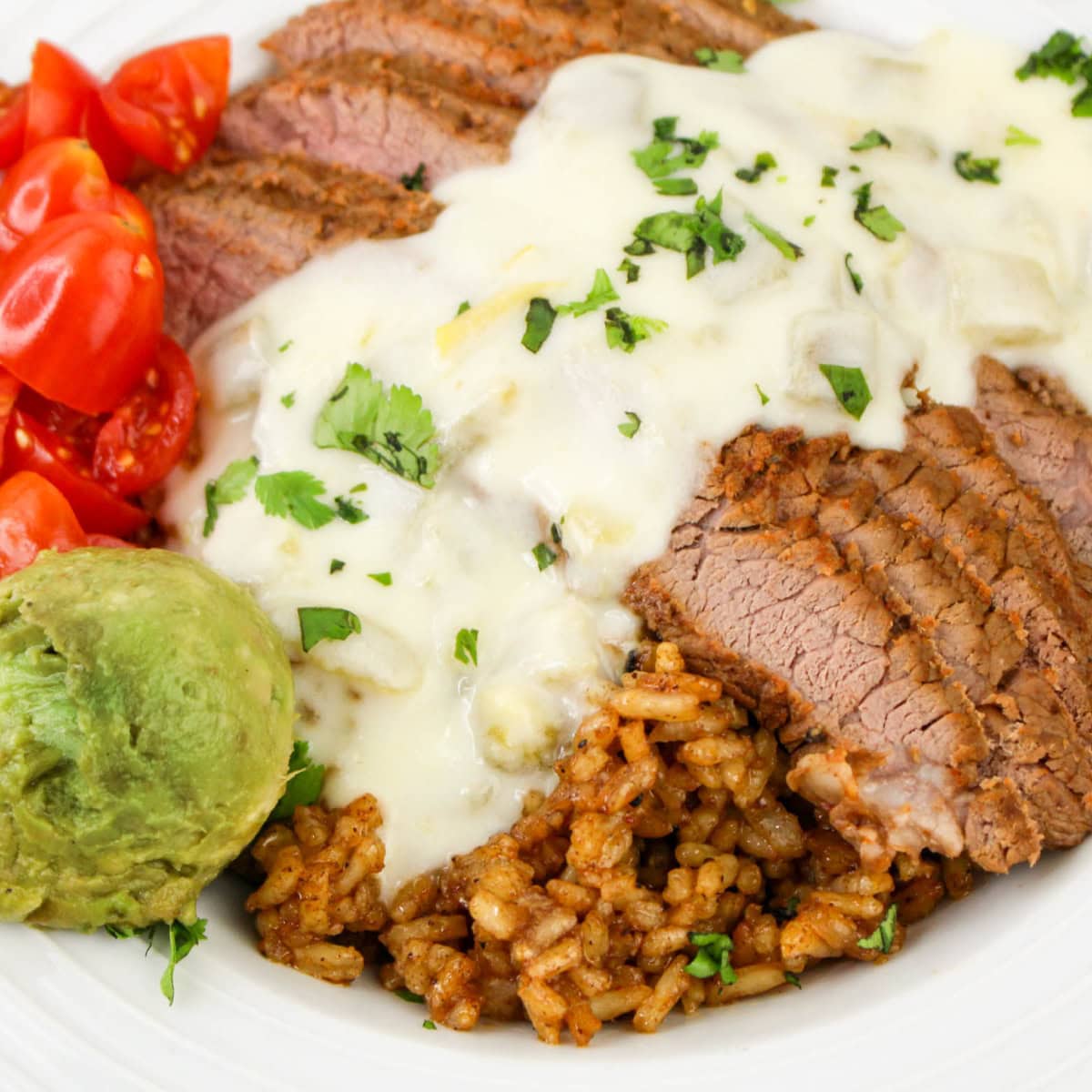 Close up view of a rice bowl with steak, guacamole, chopped tomatoes, and queso sauce.